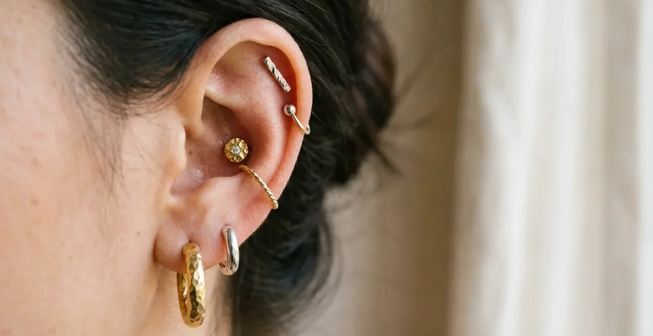 Gros plan artistique sur une oreille avec une composition harmonieuse de bijoux dorés et argentés, montrant un équilibre entre les piercings du lobe, hélix, tragus et conch