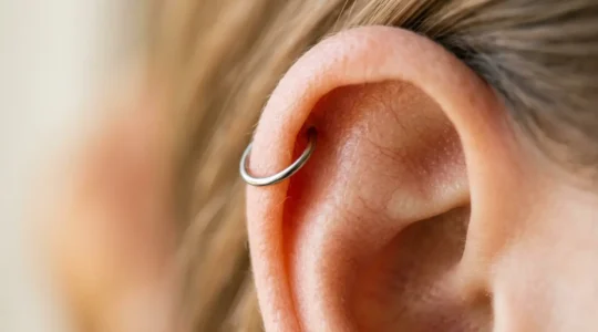 Gros plan sur une oreille avec un piercing hélix en titane brillant sur le cartilage supérieur
