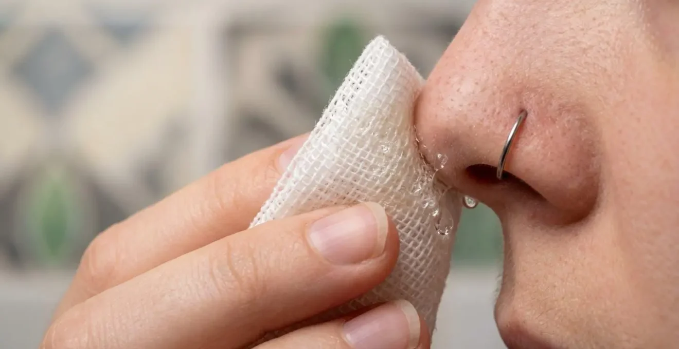 Main appliquant délicatement une compresse stérile imbibée de sérum physiologique sur un piercing nostril
