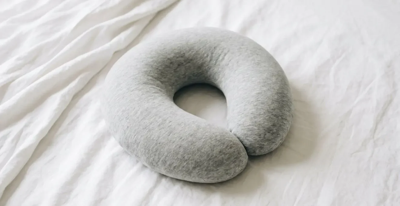 Oreiller de voyage en forme de U posé sur un lit avec drap blanc