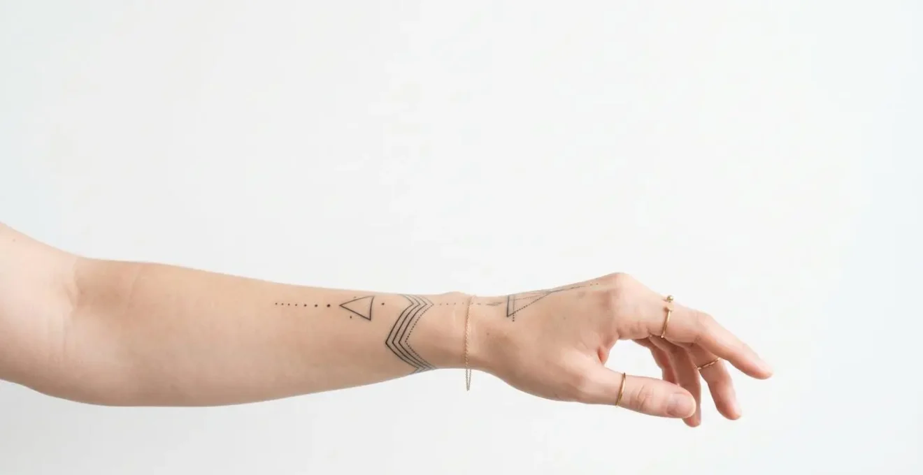 Composition minimaliste montrant des tatouages géométriques fins interagissant avec des bijoux délicats