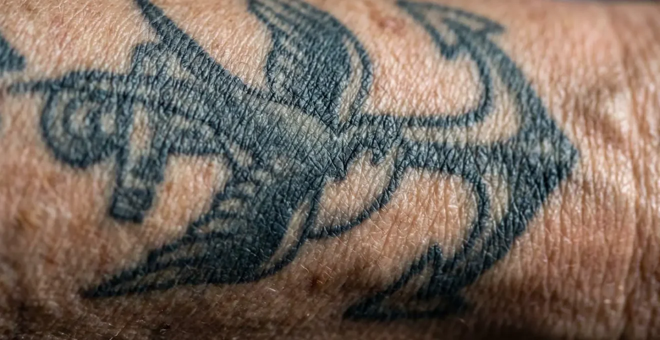 Macro détaillée montrant la texture d'un tatouage ancien sur peau mature avec patine naturelle